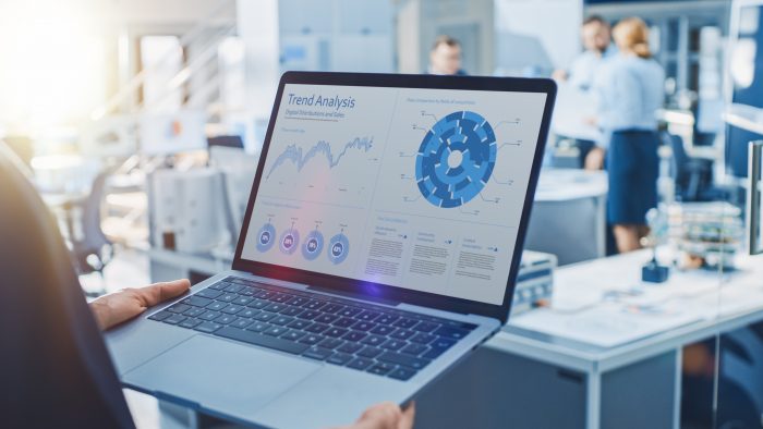 Stylish Female Industrial Robotics Engineer Uses Laptop Computer with Graphs and Diagrams in Trend Analytics Software. Technology Research Facility for Machine Learning and Cloud Computing