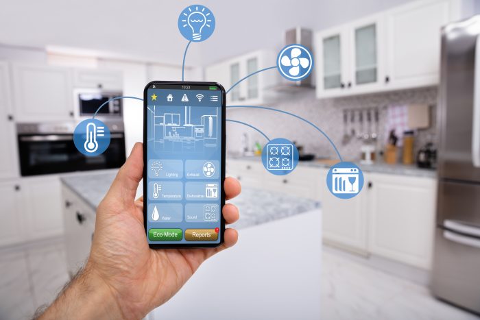 Close-up Of Man's Hand Holding Mobile With Smart Home Control Icon Feature With Kitchen Background