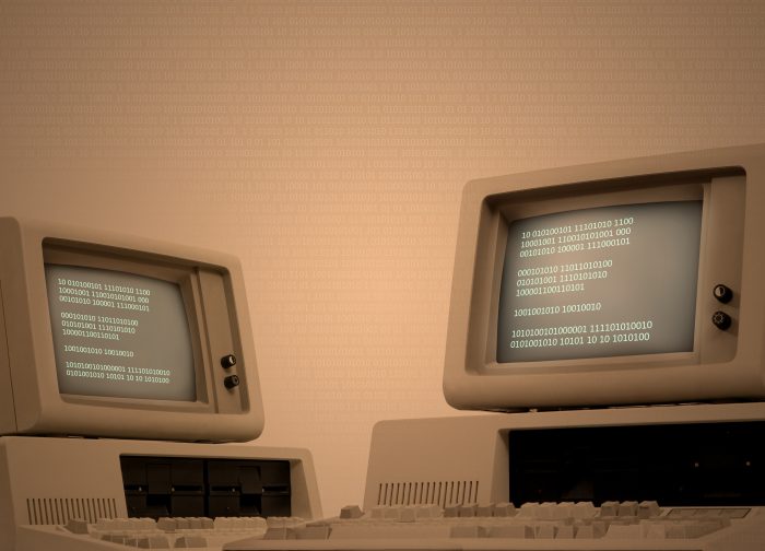 Vintage technology beige background with two old computers showing binary code on its monitor. Code spreads across image area. Retro revival of seventies devices. Plenty of copy space on the side. Low-key background for easy costumization.